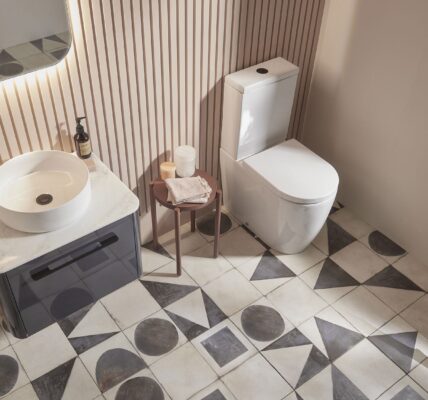 An overhead shot of a modern bathroom with a white vessel sink on a dark grey vanity, a white toilet, and patterned geometric floor tiles.
