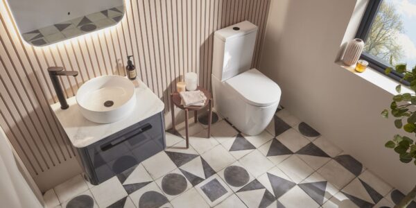 An overhead shot of a modern bathroom with a white vessel sink on a dark grey vanity, a white toilet, and patterned geometric floor tiles.