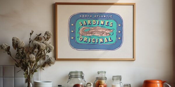 A framed illustration of a vintage sardine can label hangs on a white wall above a kitchen counter. The label features three sardines swimming in a blue oval surrounded by a light blue border.
