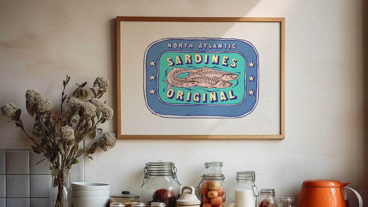 A framed illustration of a vintage sardine can label hangs on a white wall above a kitchen counter. The label features three sardines swimming in a blue oval surrounded by a light blue border.