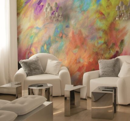 A bright, modern room features two white armchairs facing each other, with a vibrant, abstract painting-like mural on the wall behind them. The mural is a mix of swirling colours including yellow, orange, red, purple, blue, and green.