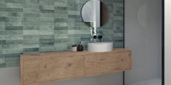 A modern bathroom interior with a focus on a stylish wall tiles. The dominant feature is the wall covered in rectangular tiles with a muted green hue. The tiles have a slightly distressed or textured appearance, adding depth and character.