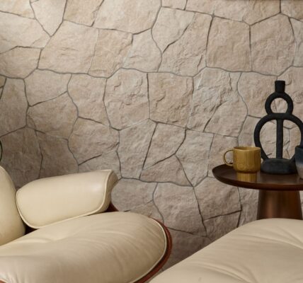 A modern living room corner featuring a cream-coloured leather armchair with a matching ottoman, positioned in front of a textured stone wall