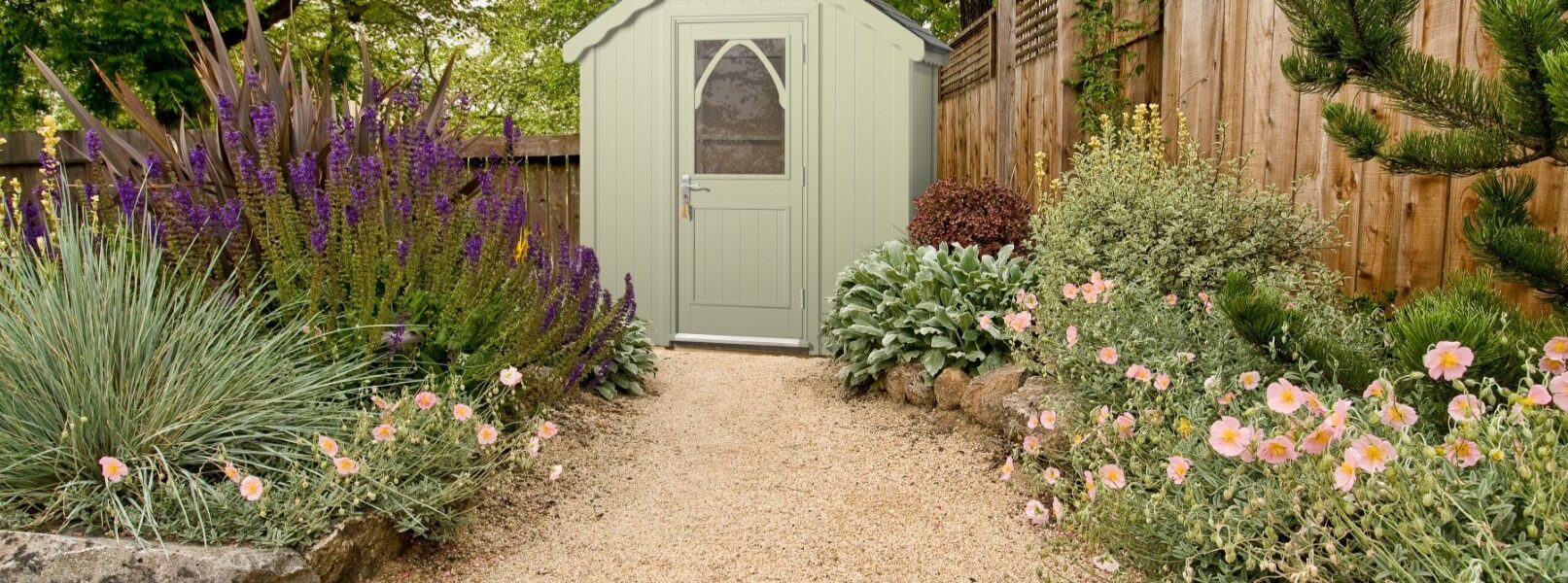 A light green wooden shed with a peaked roof and a white, arched windowed door at the far end.