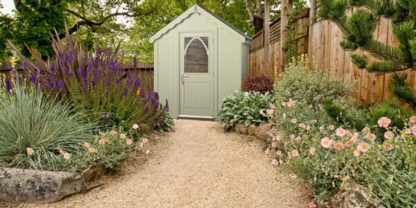 A light green wooden shed with a peaked roof and a white, arched windowed door at the far end.