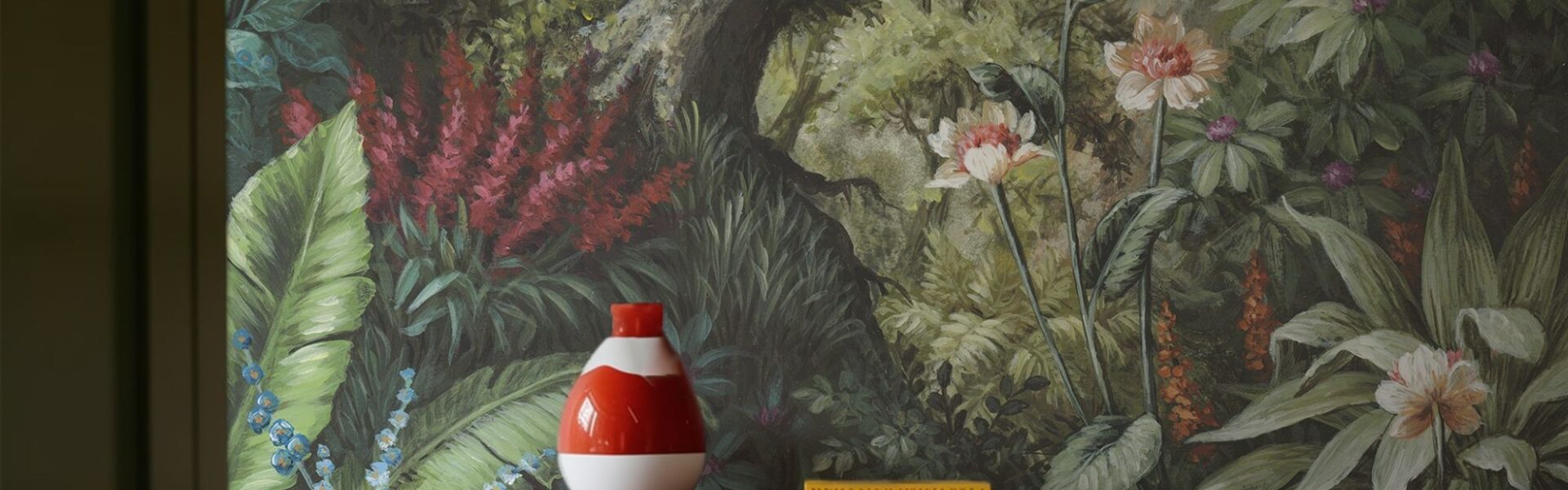 A detailed wallpaper mural depicting a lush, verdant forest scene. A tree trunk dominates the centre, surrounded by a variety of green foliage, red and white flowers.