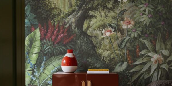 A detailed wallpaper mural depicting a lush, verdant forest scene. A tree trunk dominates the centre, surrounded by a variety of green foliage, red and white flowers.