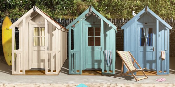 Three colourful beach hut-style sheds on a sandy surface, with surfboards and a beach chair nearby
