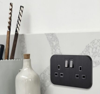 A sleek, black double UK plug socket (13A) is mounted on a grey and white marble-effect splashback in a modern kitchen.