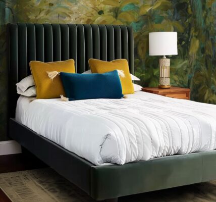 A beautifully styled bedroom features a bed with a dark green upholstered headboard and a matching green bed frame. The wall behind the bed is adorned with a lush, nature-inspired wallpaper mural in shades of green and yellow, giving the room a vibrant, organic feel.
