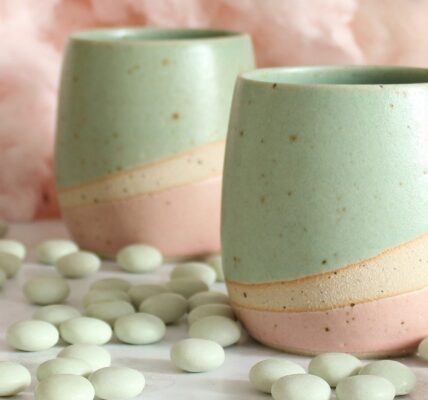 Two pastel-coloured ceramic tumblers, a light mint green on top and a soft pink on the bottom, with a creamy beige stripe separating the two colours.