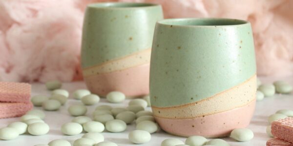 Two pastel-coloured ceramic tumblers, a light mint green on top and a soft pink on the bottom, with a creamy beige stripe separating the two colours.