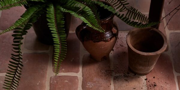 The image shows a close-up, overhead view of a rustic-looking floor made of reddish-brown terracotta tiles, laid in a brick-like pattern.