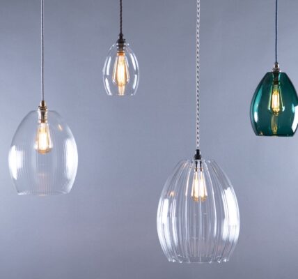 A studio shot of four pendant lights with various glass shades. All lights are hanging against a grey background.