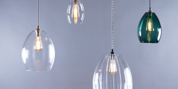 A studio shot of four pendant lights with various glass shades. All lights are hanging against a grey background.