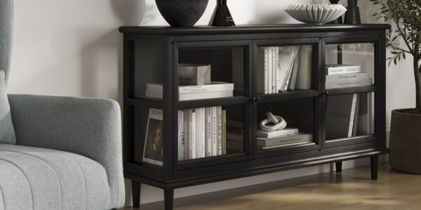 A sleek, modern black sideboard with three glass-fronted doors, each revealing two shelves filled with books and decorative objects.