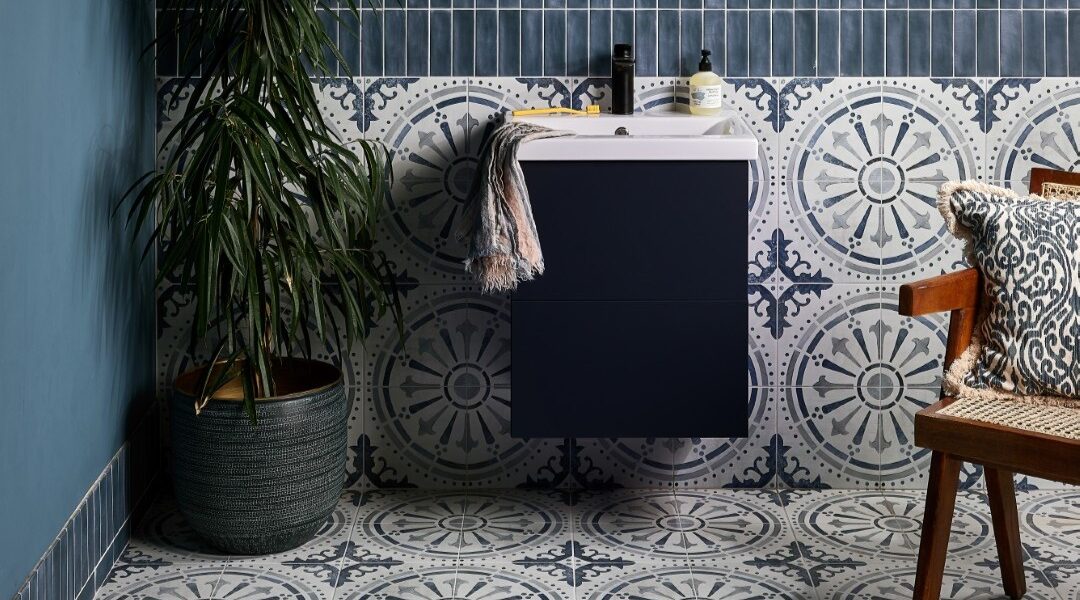 The wall features two types of tiles: a dark blue, possibly subway-style, tile on the upper part, and a patterned tile with a circular, almost mandala-like design in shades of blue and white on the lower half. This same patterned tile extends across the entire floor.
