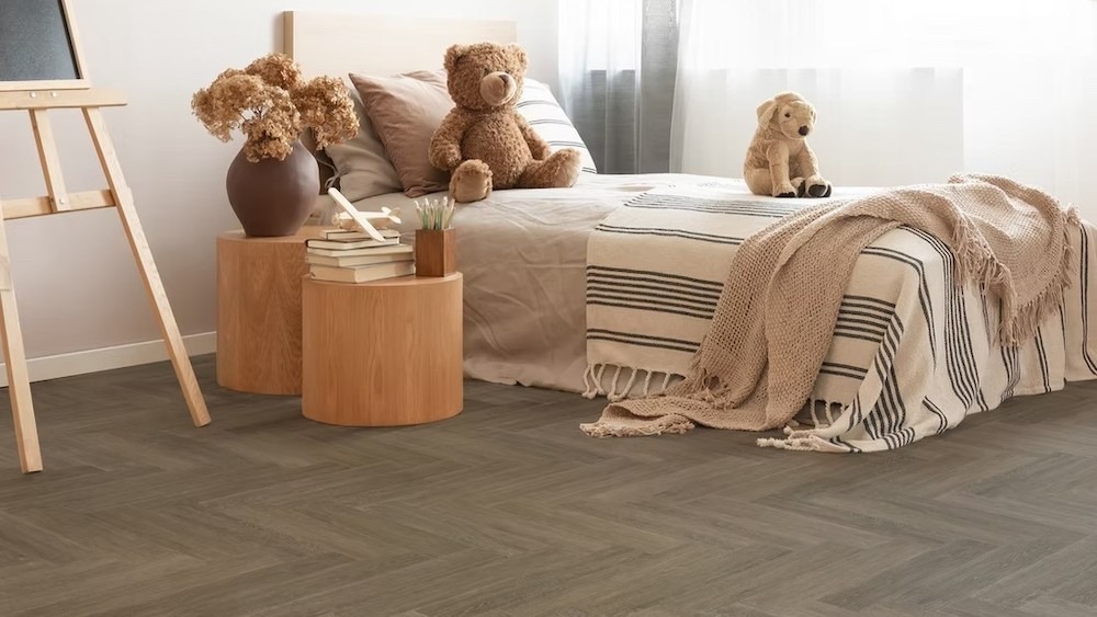A child's bedroom with a neutral and warm aesthetic. The flooring is a dark, herringbone-patterned vinyl plank.