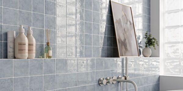 A bathroom scene featuring light blue, square wall tiles with a glossy, uneven surface. The tiles are arranged in a grid pattern with white grout lines.