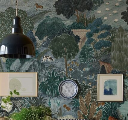 A beautifully decorated room featuring a wall adorned with a whimsical, illustrative wallpaper depicting a pastoral scene. The wallpaper, in shades of blue, green, and brown, shows rolling hills, trees, a bridge, and various animals like horses, sheep, and a cow.