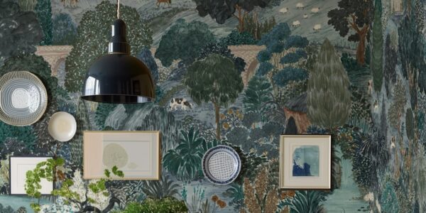 A beautifully decorated room featuring a wall adorned with a whimsical, illustrative wallpaper depicting a pastoral scene. The wallpaper, in shades of blue, green, and brown, shows rolling hills, trees, a bridge, and various animals like horses, sheep, and a cow.