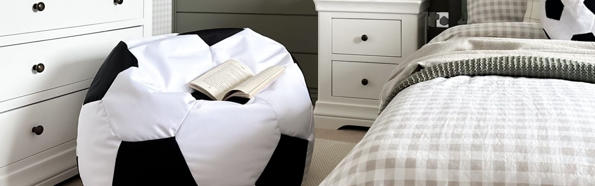 A large, white and black soccer ball-shaped bean bag sits on a light-coloured rug in a bedroom.