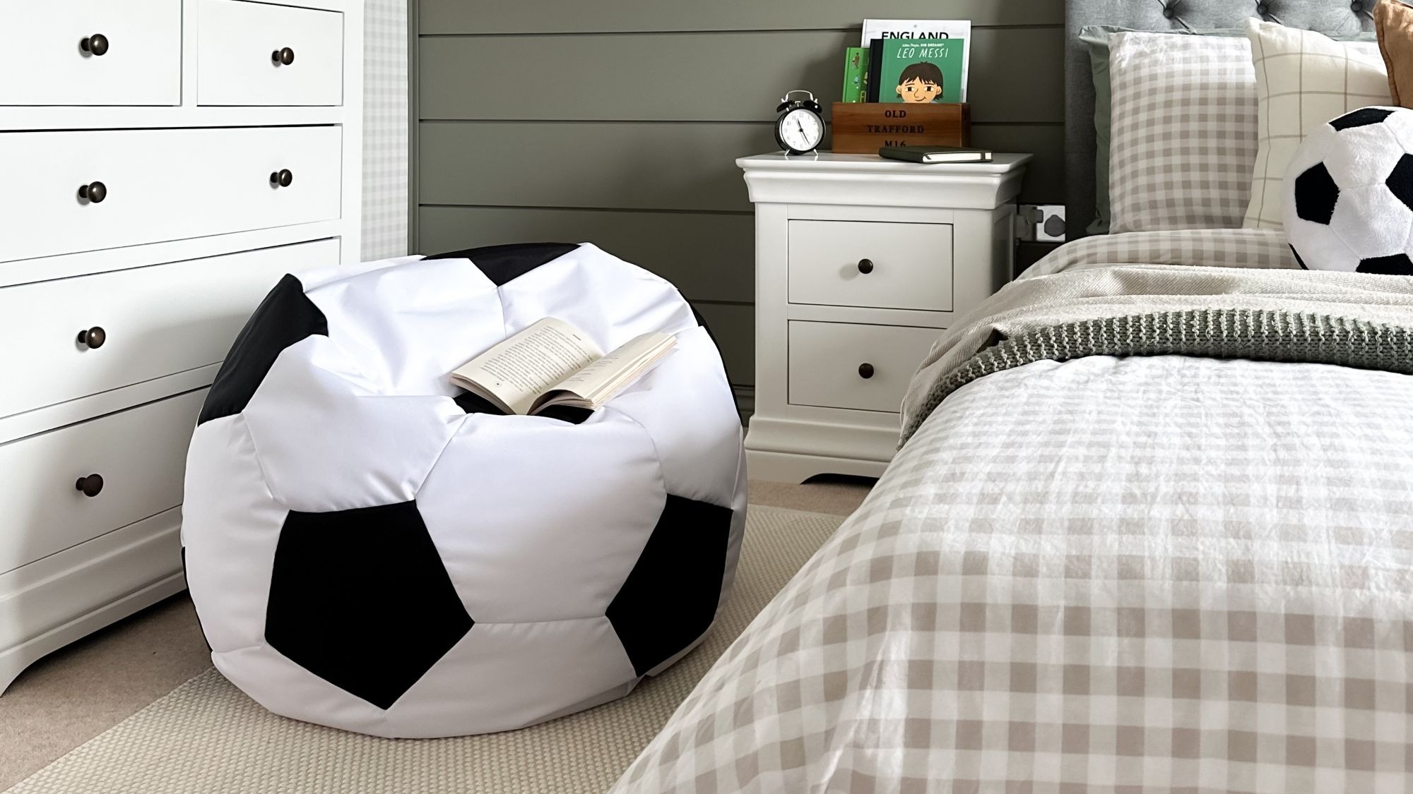A large, white and black soccer ball-shaped bean bag sits on a light-coloured rug in a bedroom.