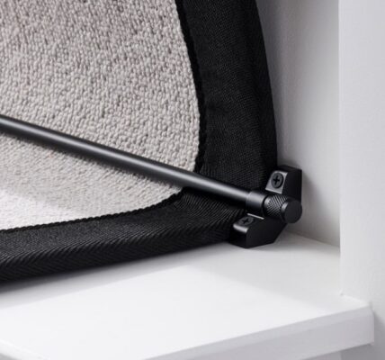 A close-up, low-angle shot of a black stair carpet runner rod installed on a white staircase. The black runner rod is held in place by a matching black bracket on the left, which is screwed into the white stair riser. The bracket has a decorative knob on the front, and the screw is visible.