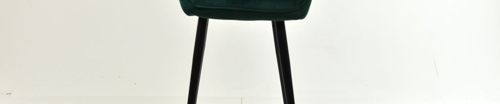 A single, modern bar stool with a deep green, vertically channel-tufted velvet seat and backrest, resting on tall, slim black wooden legs.