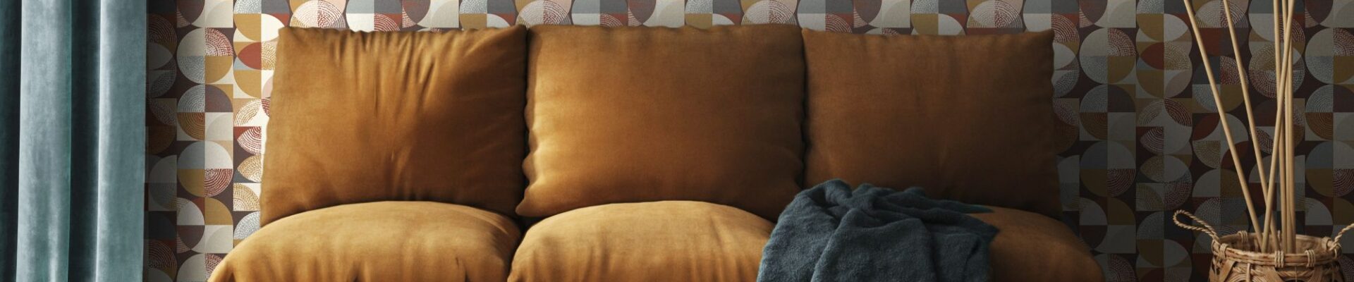 A living room with a three-seater sofa, wooden parquet flooring and denim blue curtains. The background features a geometric wallpaper in different shades of brown, orange and amber