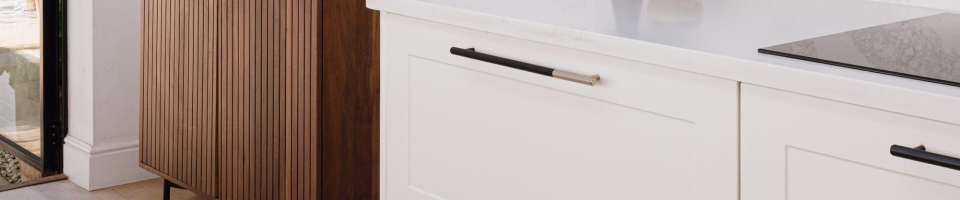 This image shows white kitchen cabinets with recessed panels. The cabinets are fitted with long, linear cabinet handles that have a two-tone finish - black with a silver tip. A white countertop sits above the cabinets.