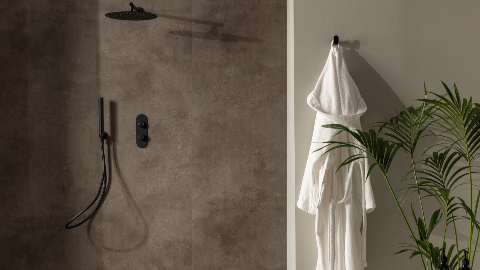 A shower wall clad in a dark, mottled, stone-effect panel. It has a warm, earthy brown/grey tone with slight texture variations. The shower fixtures—including the rainfall shower head, the handheld shower wand, and the control panel—are all in a matte black finish, providing a stark, contemporary contrast against the stone panel.