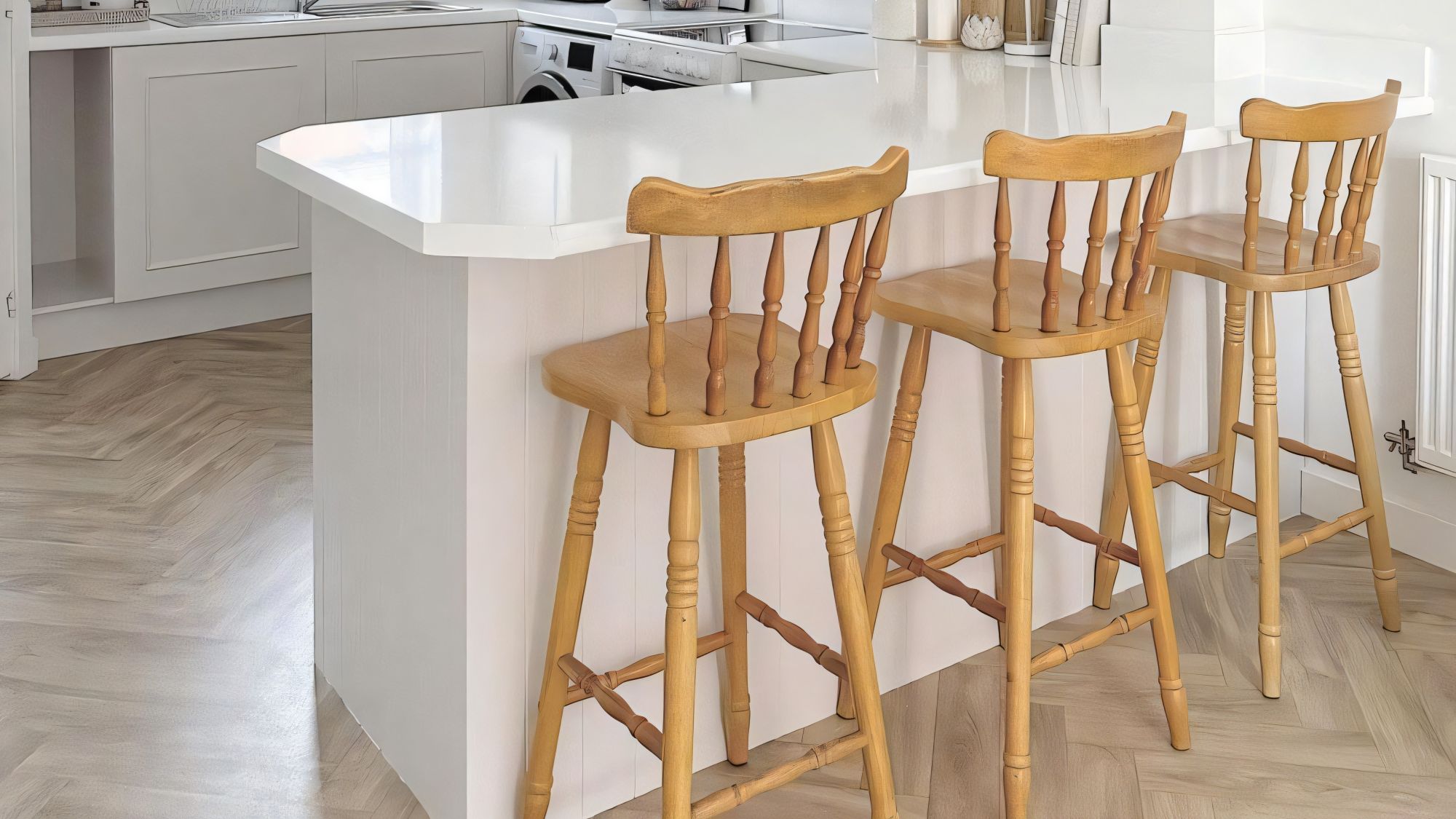 A white kitchen island or breakfast bar with a clean, white countertop. The side facing the viewer appears to be finished with white vertical panelling - possibly V-groove or tongue and groove style.
