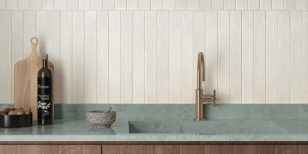 An eye-level, horizontal shot of a modern, minimalist kitchen features a vertical stack-bond backsplash made of textured, off-white rectangular tiles.