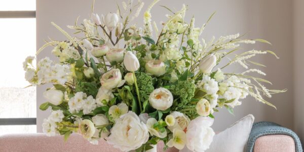 A lush, large floral arrangement in a white ceramic vase featuring a mix of white and cream-coloured flowers