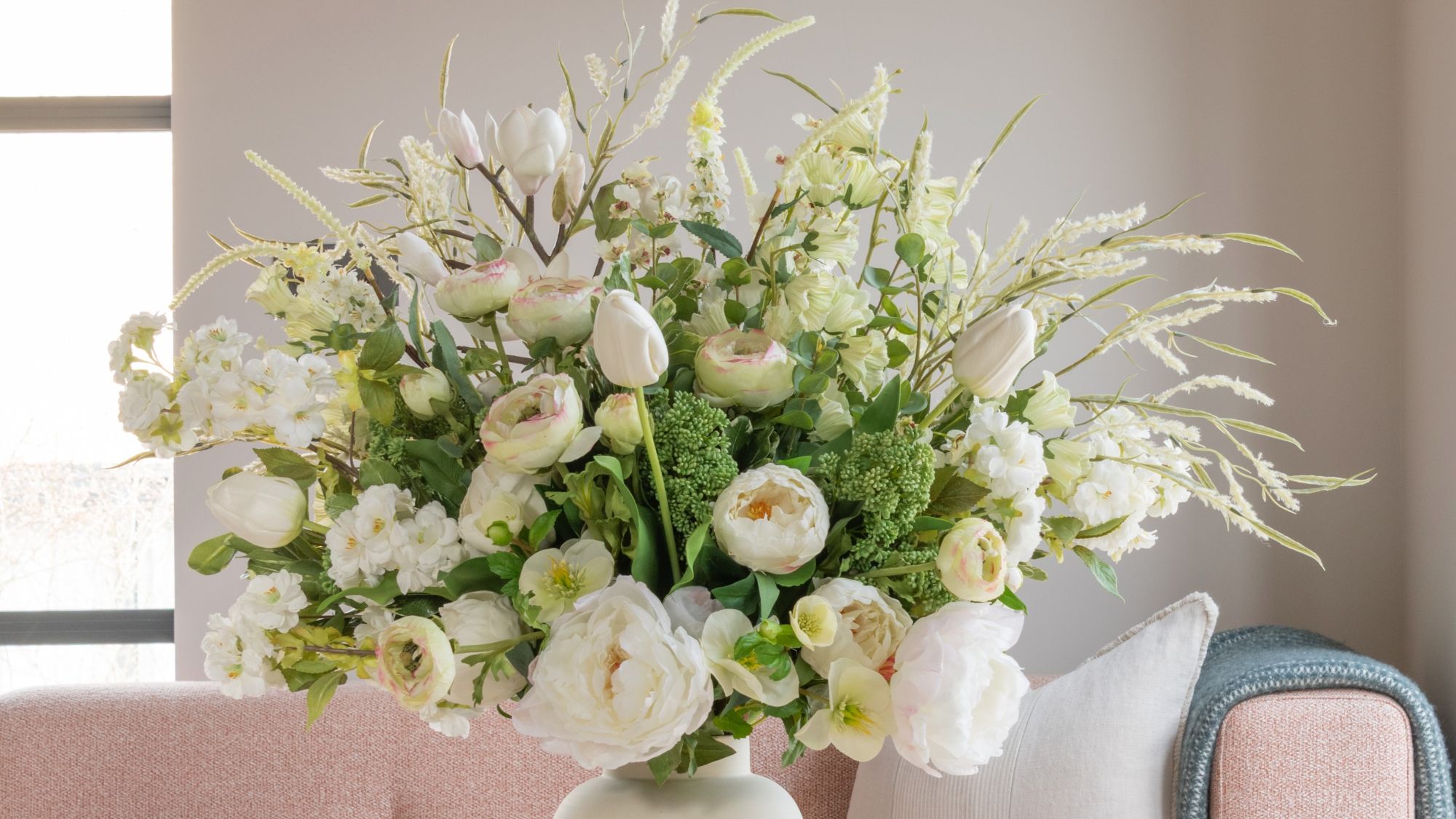 A lush, large floral arrangement in a white ceramic vase featuring a mix of white and cream-coloured flowers