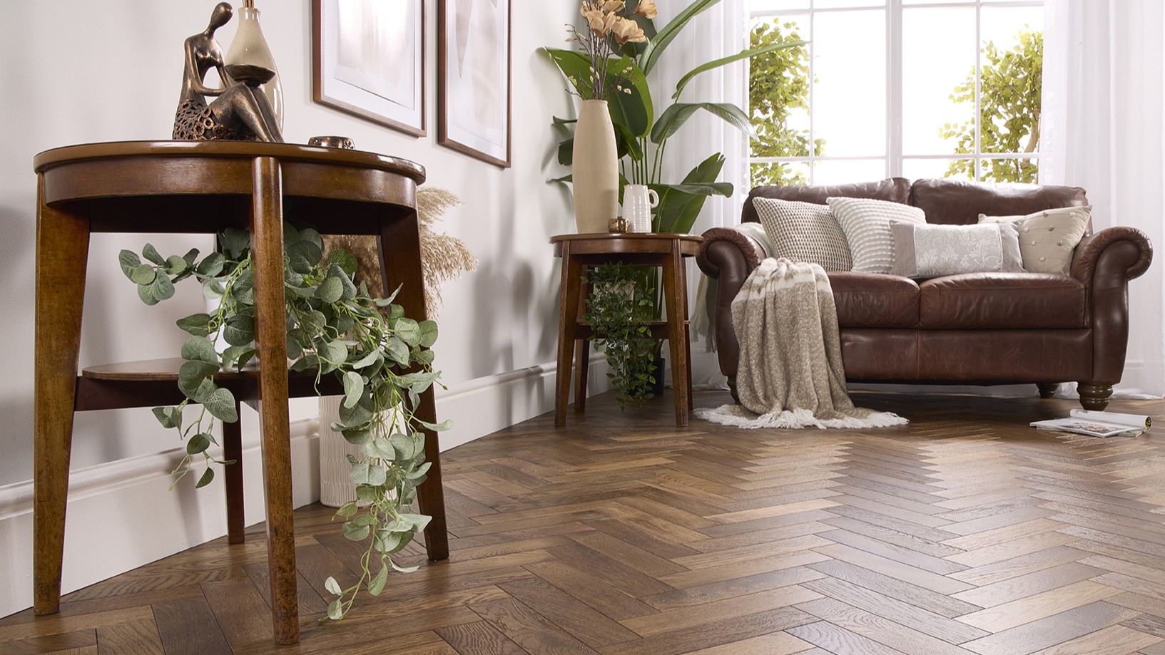 Alston Double Smoked herringbone engineered oak flooring in a brightly lit, modern living room with a brown leather sofa and wooden side tables