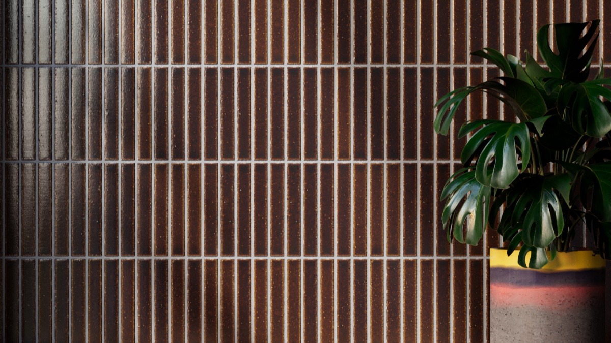 Vertically stacked Kaji Border Japanese porcelain tiles in burnt russet brown with light grout, featured behind a potted Monstera plant.