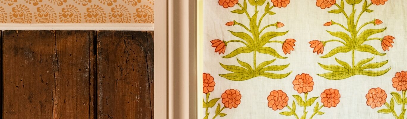 A window with a white frame and a white curtain with orange flowers on it Description automatically generated
