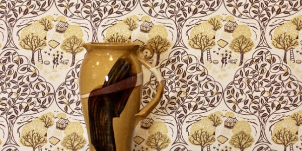 A wallpaper behind a vase which depicts a charming countryside scene and is available in seven colourways.