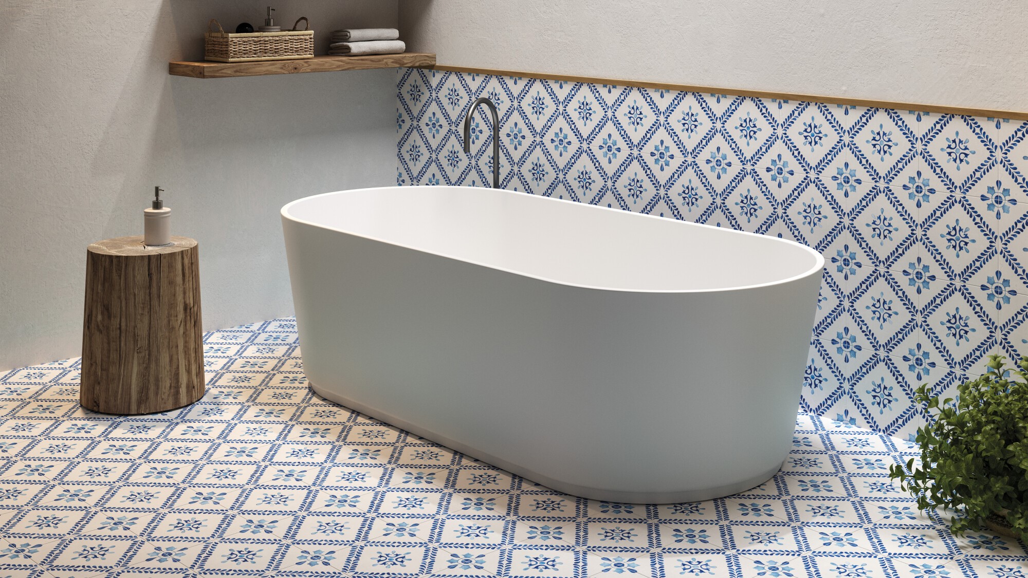 The image shows a modern bathroom setting with a focal point on a standalone bathtub. The bathtub is white with a smooth, curved design, likely made of acrylic or porcelain, and it's positioned in the centre of the room. Behind the tub, there is a section of the wall decorated with blue and white patterned tiles that add a traditional and somewhat Mediterranean touch to the space. The floor is adorned with matching tiles, creating a cohesive and vibrant aesthetic. To the left of the tub, there's a wooden stool that holds a dispenser bottle, possibly soap or lotion. Above the bathtub, a wooden shelf stretches across the wall, holding neatly stacked towels and some bathroom essentials in a wicker basket. On the right side, there is a green plant that introduces a natural element and a pop of colour to the scene. The overall look of the bathroom is clean, serene, and stylish, with a blend of modern fixtures and classic decorative tiles.