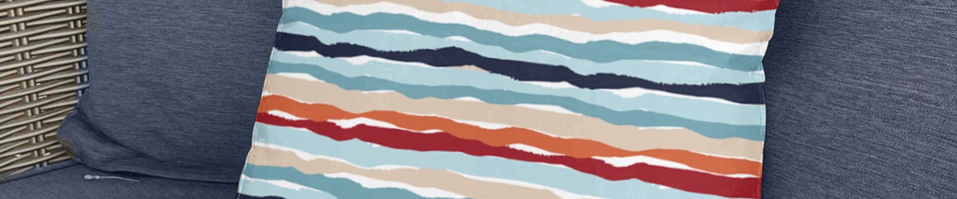A square, coral and white striped throw pillow sits on a couch with a blue and white striped pattern.