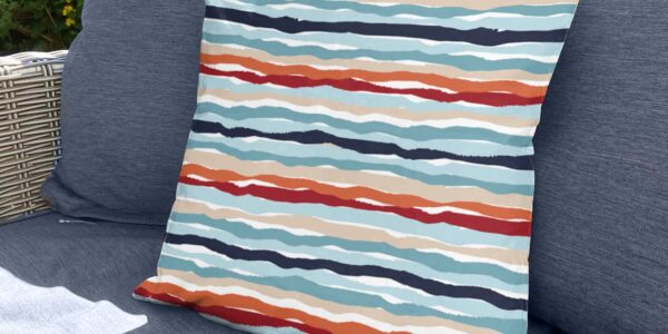 A square, coral and white striped throw pillow sits on a couch with a blue and white striped pattern.