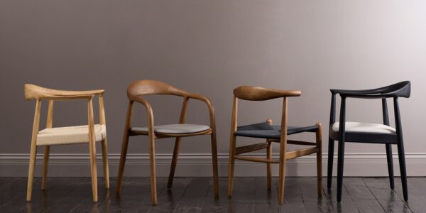 Four wooden chairs with brown upholstery in a row on a light wooden floor. The chairs are against a plain light wall.