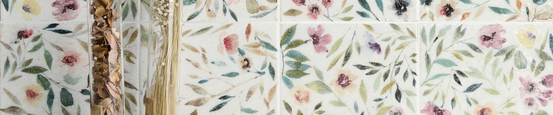 A close-up of a square white tile with a floral pattern in shades of blue and green.