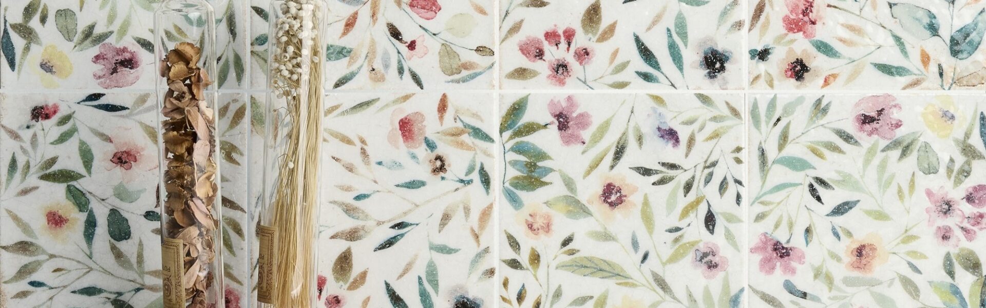 A close-up of a square white tile with a floral pattern in shades of blue and green.