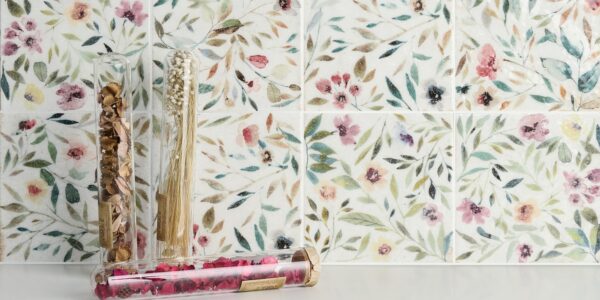 A close-up of a square white tile with a floral pattern in shades of blue and green.