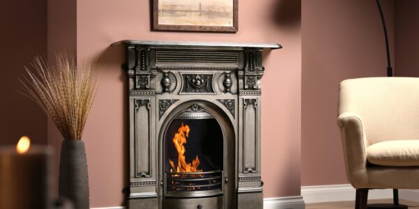 A cast iron fireplace with a fire burning in the grate. The fireplace is in a living room with an armchair next to it.