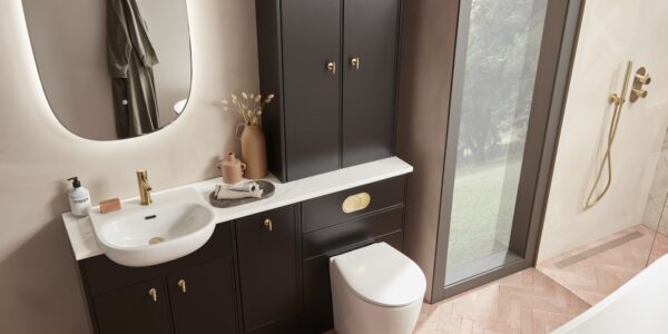A bright and clean bathroom with a sink, toilet, and mirror. The bathroom has white walls and a tiled floor. There is a window on the left wall. In the foreground, there is a small plant on the sink counter.