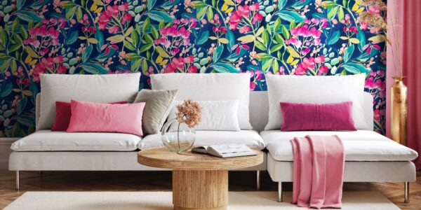 Living room with colourful floral wallpaper on one wall and a pink couch with a round coffee table in front of it. There is a white lamp on the coffee table and a green plant behind the couch.
